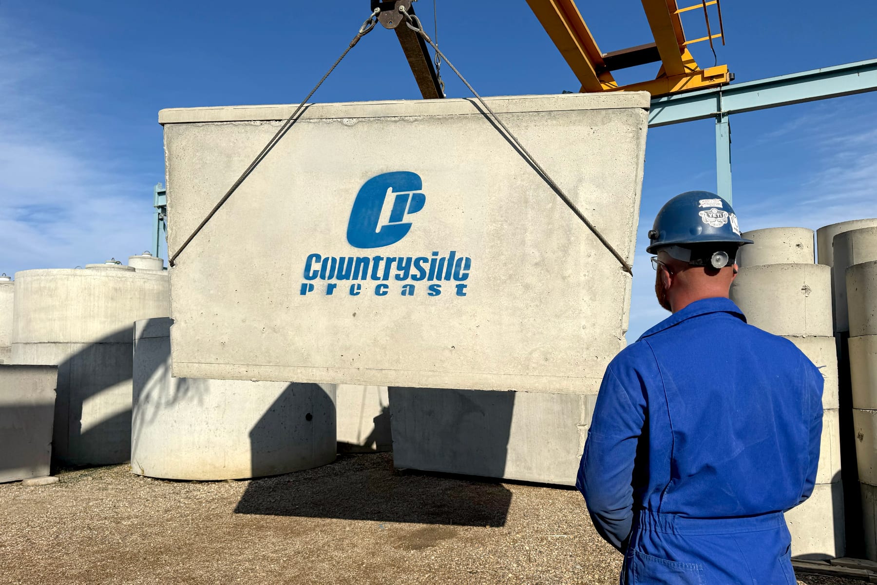 A Countryside Precast crew member watching a logo-stencilled tank panel move on the shop crane